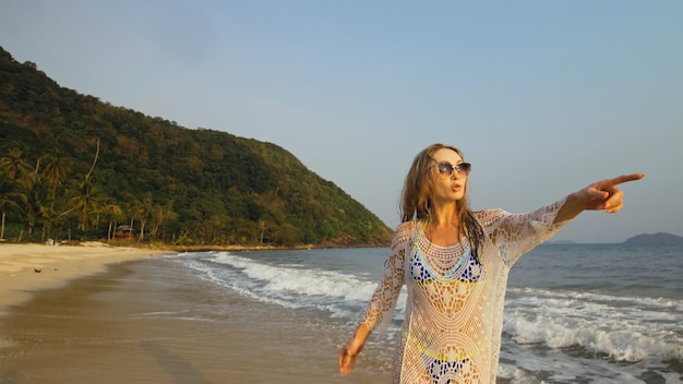 Donna in una tunica bianca sulla spiaggia vicino al mare in tempesta Bionda