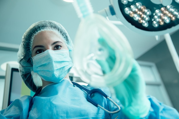 Donna in uniforme medica in piedi con una maschera per narcosi in mano