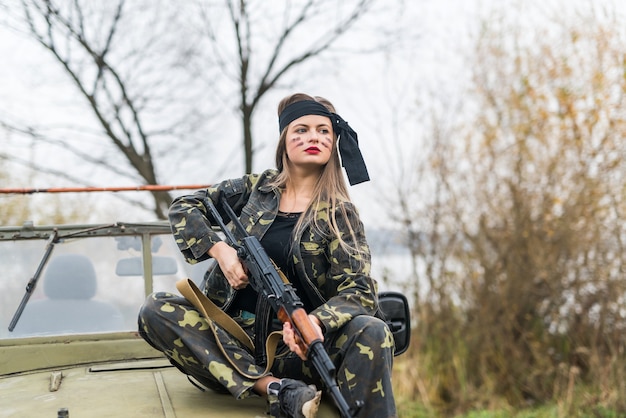 Donna in uniforme militare con fucile e auto