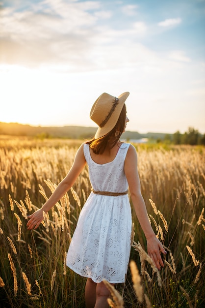 Donna in vestito che cammina nel campo di grano sul tramonto