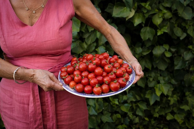 Donna in vestito rosa che tiene un piatto pieno di pomodorini rossi freschi