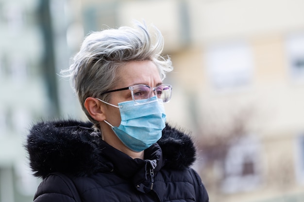 Donna in via della città che indossa una maschera protettiva per la diffusione del virus della malattia