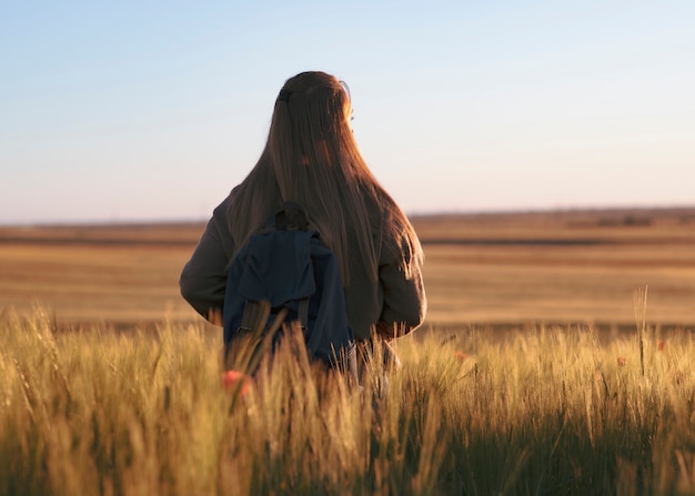 Donna in viaggio con zaino. è nel campo a guardare il tramonto, campo di grano d'orzo