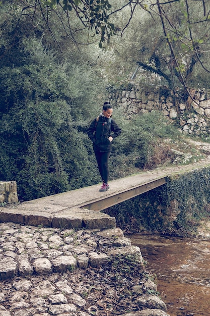 Donna in viaggio in piedi sul ponte di pietra e guardando il flusso d'acqua nei verdeggianti boschi di Maiorca