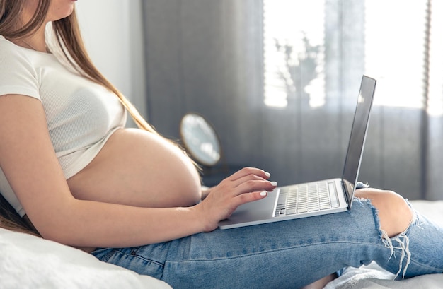 Donna incinta a letto nell'interiore della stanza con il computer portatile
