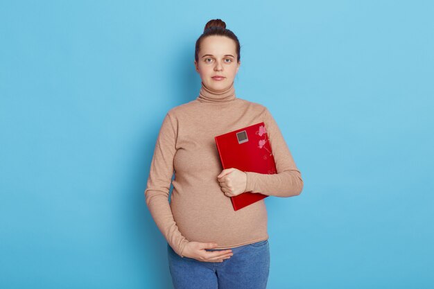 Donna incinta abbastanza giovane che tiene una scala rossa nelle mani