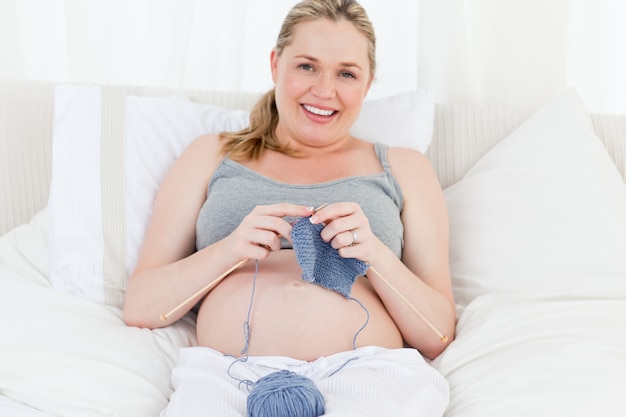 Donna incinta adorabile che lavora a maglia sul suo letto