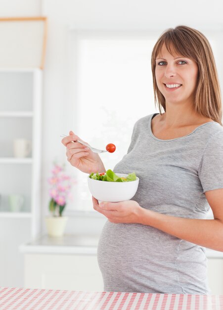 Donna incinta affascinante che mangia un pomodoro ciliegia mentre stando