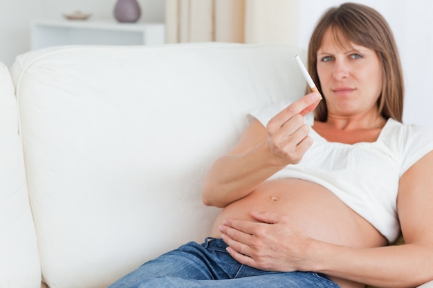 Donna incinta affascinante che tiene una sigaretta mentre trovandosi su un sofà