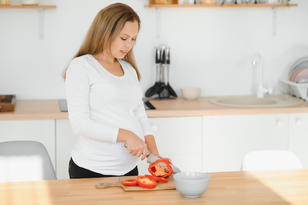 Donna incinta affettare le verdure a casa in cucina