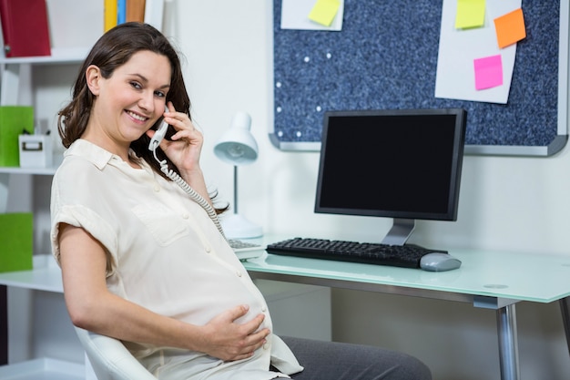 Donna incinta al telefono alla scrivania