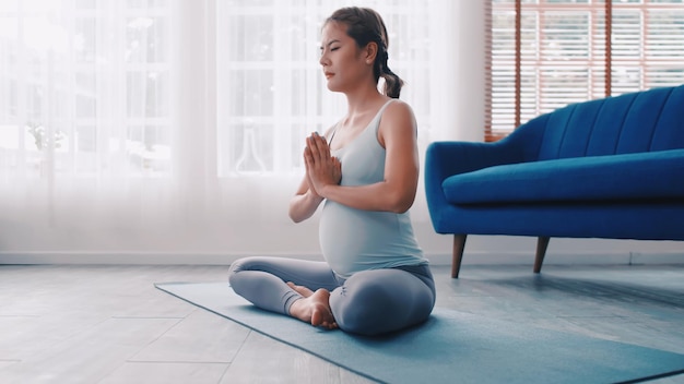 Donna incinta asiatica che fa esercizi di yoga a casa.