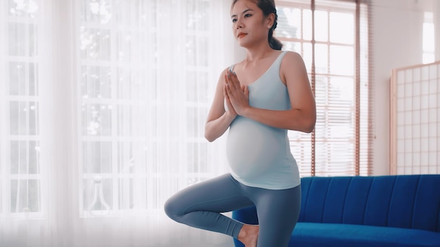 Donna incinta asiatica che fa esercizi di yoga a casa.