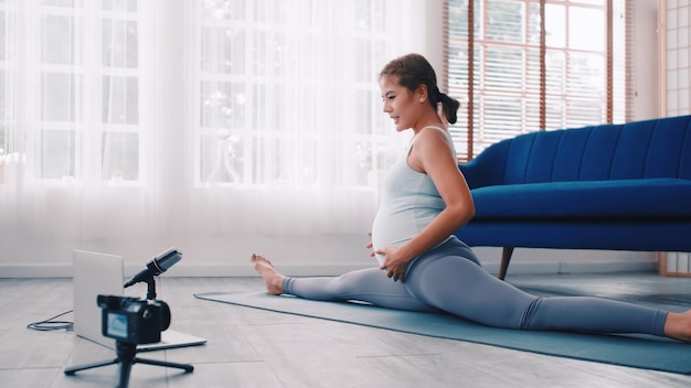 Donna incinta asiatica che insegna esercizi di Pilates online a casa.