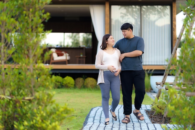 Donna incinta asiatica con suo marito che camminano insieme in giardino a casa
