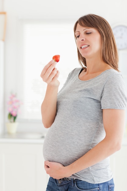 Donna incinta attraente che mangia una fragola mentre stando