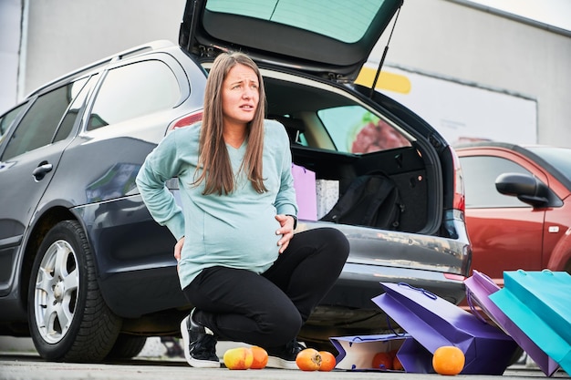 Donna incinta che cerca di raccogliere frutta sparsa nel parcheggio