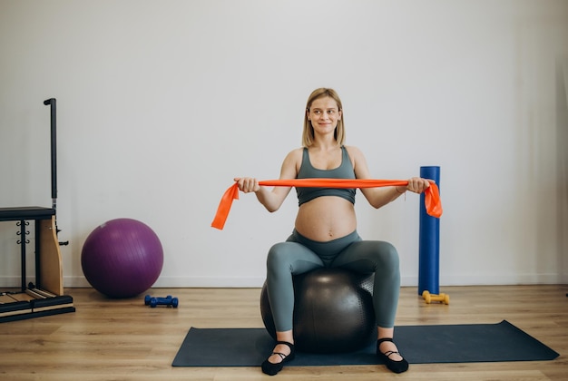 Donna incinta che fa esercizi di rilassamento con una palla di pilates fitness a casa
