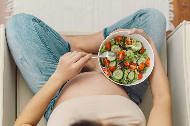 Donna incinta che gode dell'insalata della verdura fresca.