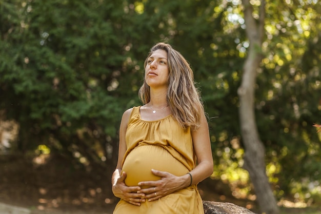 Donna incinta che guarda da un'altra parte mentre si trova contro gli alberi