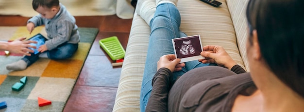 Donna incinta che guarda l'ecografia del suo nuovo bambino mentre il fratello maggiore gioca