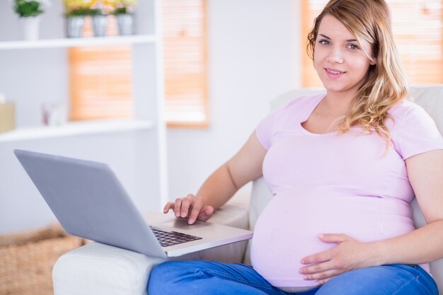 Donna incinta che guarda l&#39;obbiettivo e usando il portatile