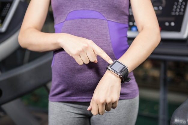 Donna incinta che indica orologio astuto alla palestra