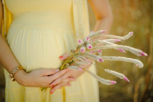 Donna incinta, che indossa un abito giallo chiaro, tenendo in mano un bouquet di fiori di margherita.