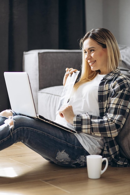 Donna incinta che lavora al computer portatile e che beve caffè