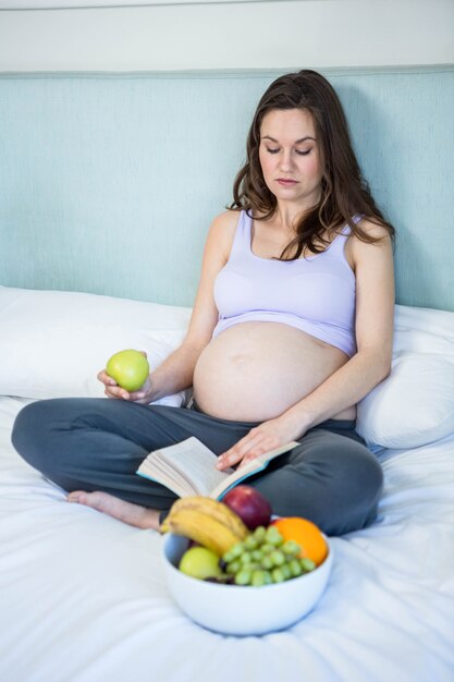 Donna incinta che legge un libro che si trova sul suo letto