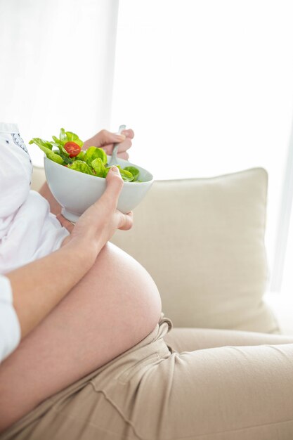 Donna incinta che mangia insalata sul divano