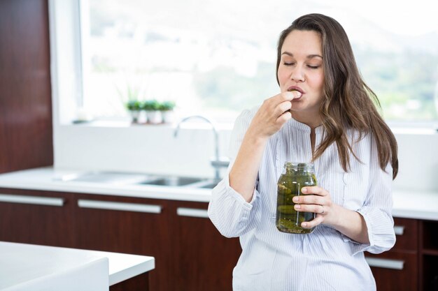 Donna incinta che mangia sottaceti in cucina