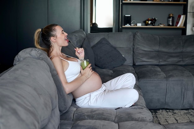 Donna incinta che mangia un frullato nel soggiorno Pre sano