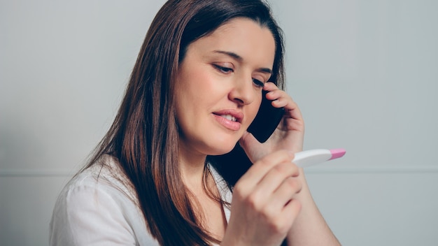 Donna incinta che parla al telefono cellulare che sembra positivo al test di gravidanza