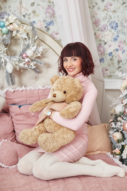Donna incinta che posa sul letto con un orsacchiotto