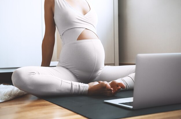 Donna incinta che pratica yoga a casa con il computer portatile L'esercizio femminile medita durante la gravidanza