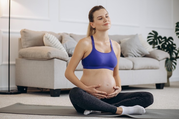 Donna incinta che pratica yoga a casa sul tappetino