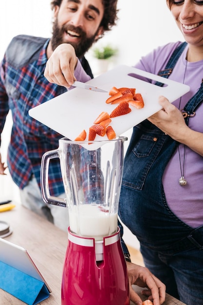 Donna incinta che prepara frullato con fragole fresche, vista parziale