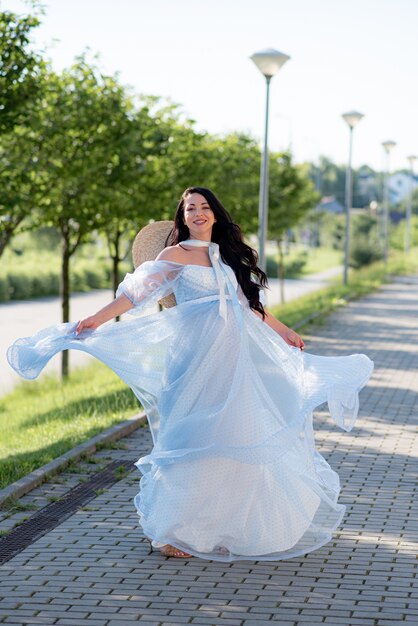 Donna incinta che propone in un vestito blu su una priorità bassa degli alberi verdi