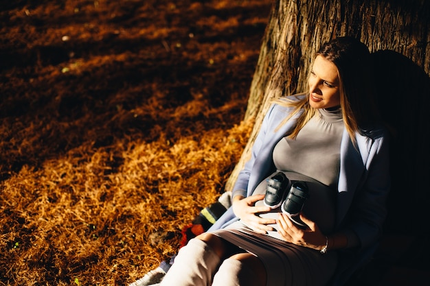 Donna incinta che si siede sotto l&#39;albero di autunno