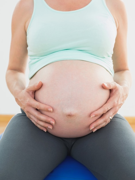 Donna incinta che si siede sulla sfera blu di esercitazione che tiene la sua pancia