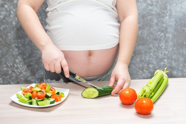 Donna incinta che taglia cetriolo per insalata verde fresca, femmina prepara una gustosa cena biologica a casa.