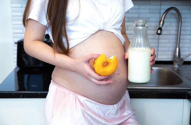 Donna incinta che tiene Bottiglia di latte e ciambella dolce Cibo sano durante la gravidanza