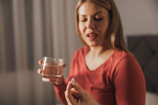 Donna incinta che tiene il bicchiere con acqua e beve pillola di vitamina al mattino.