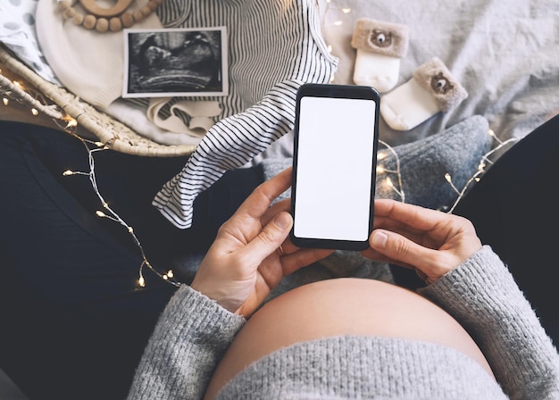 Donna incinta che tiene in mano smartphone con display bianco vuoto