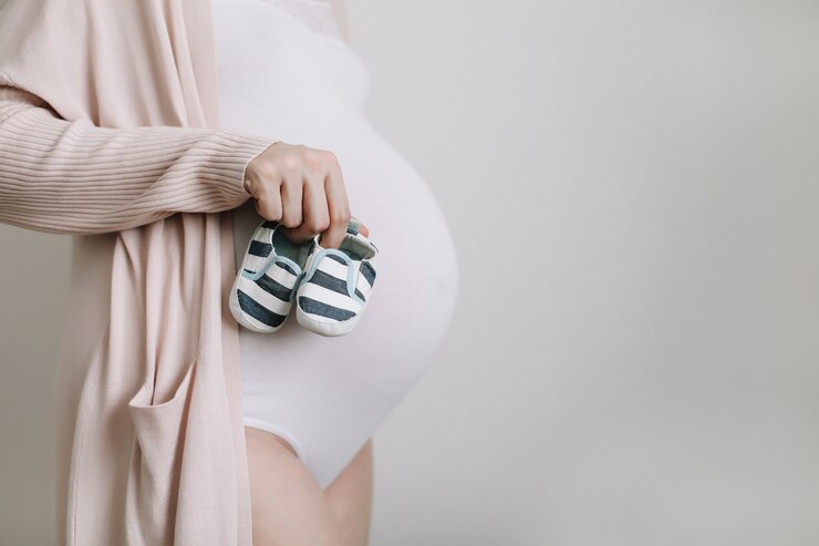 donna incinta che tiene le scarpe per il neonato