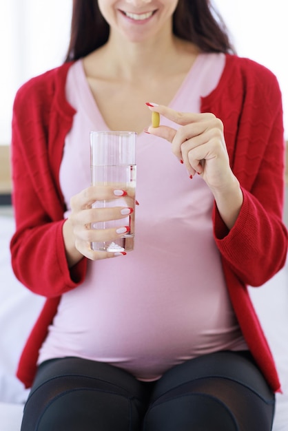 Donna incinta che tiene un bicchiere d'acqua e prende le pillole in mano per nutrire il suo corpo