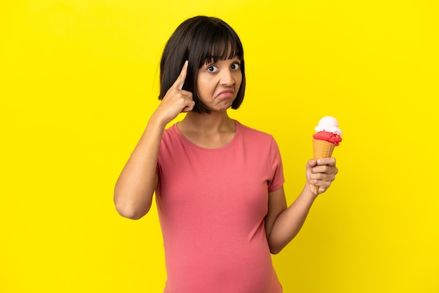 Donna incinta che tiene un gelato alla cornetta isolato su sfondo giallo pensando a un'idea