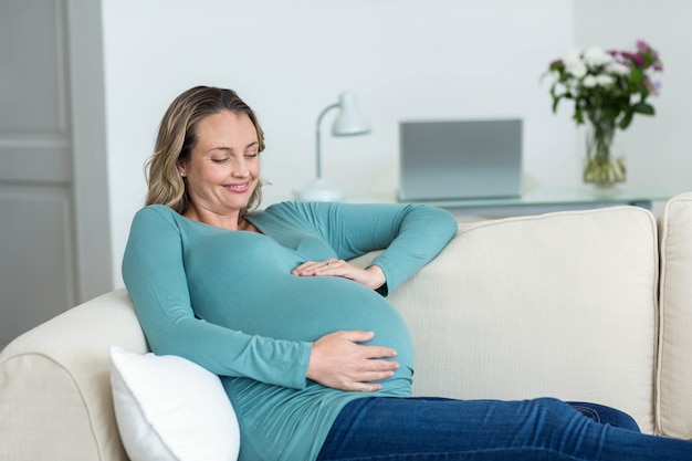 Donna incinta che tocca la sua pancia sdraiata sul divano