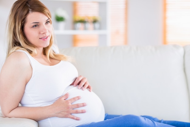 Donna incinta che tocca la sua pancia sul divano